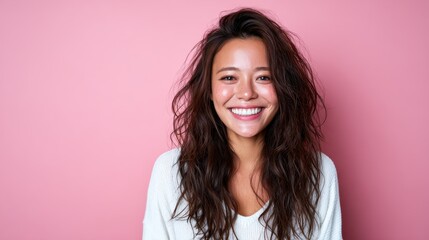 Fototapeta premium A cheerful young woman with curly hair smiles radiantly against a soft pink background, representing happiness, beauty, and the joy of living in a vibrant atmosphere.