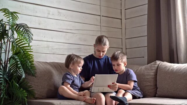 Child guides sibling peacefully at home. Young girl tutors brother quietly indoors alongside houseplant. Gentle sister instructs brother with focused reading amid cozy furniture setting