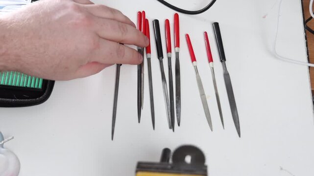 Top view of a tattooed craftsman arranging a set of mini needle files on a white workbench