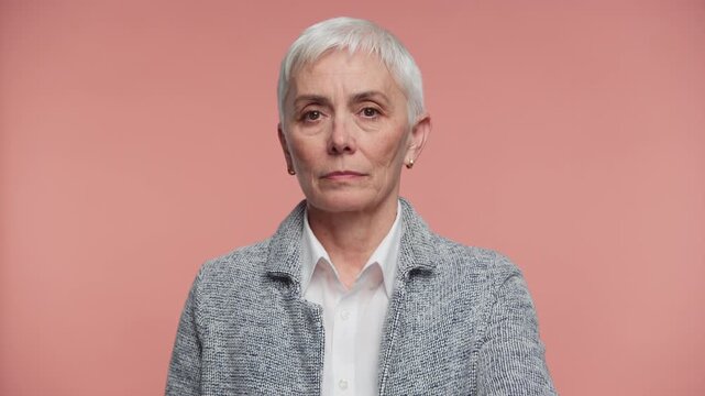 Senior woman making stop hand gesture on pink background
