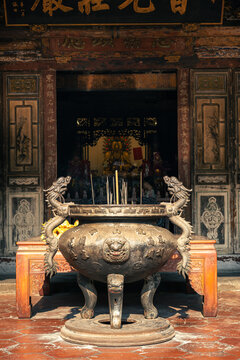 Large traditional bronze incense burner with dragon handles and burning joss sticks in front of a Chinese temple altar with a golden deity statue in Taichung Taiwan