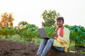 Young Indian farmer using a laptop in an agricultural field, showcasing smart farming and digital agriculture at sunset. © Niks Ads