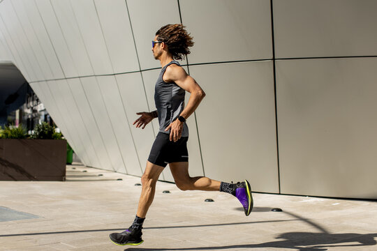 Runner sprinting under bright sun with modern architecture behind