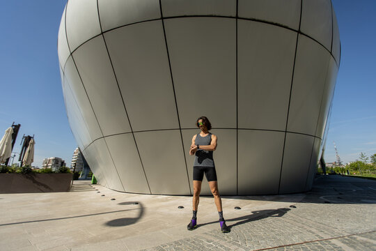 Runner stretches under a modern architectural structure on a sunny day