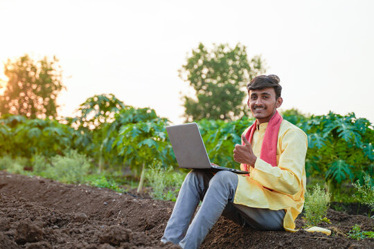Young Indian farmer using a laptop in an agricultural field, showcasing smart farming and digital agriculture at sunset.
