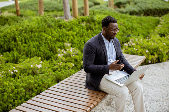 Man sitting on bench using laptop in green park during daytime work session