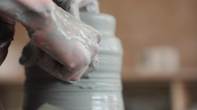 Closeup caucasian hands refining clay lip on spinning wheel in pottery studio, thumb smoothing rim of jar, steady rotation, warm workshop shelves in soft focus, patient craft practice