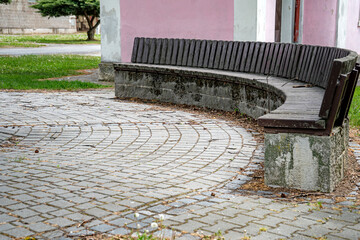 Obraz premium Curved wooden bench on paved village square near historic chapel drevena lavice obec Blatec, Czech Republic - May 10, 2026