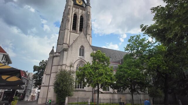 Historic Gothic church tower rising in a smooth tilt‑up view of Sint‑Maartenskerk in Kortrijk, Belgium, showing stone detail and vertical architecture.
