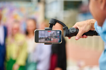Hand holding smartphone stabilizer filming group of people outdoors in daylight © TRAVELARIUM