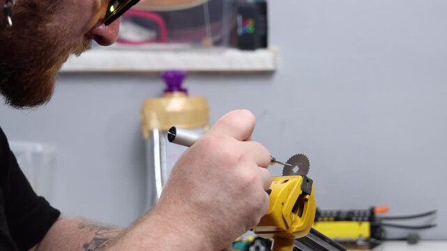 Bearded craftsman using a mini rotary tool to process a metal blade in a vise