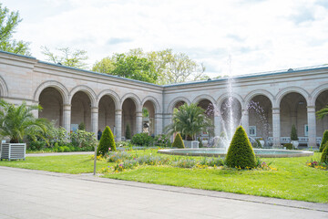 Obraz premium Scenic view of park fountain through stone arcade. Beautiful classical colonnade gallery with garden