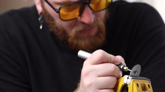 Bearded craftsman in yellow safety glasses operating a precision rotary tool on a blade