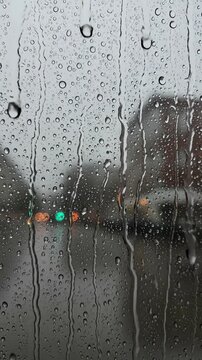 Rainy day traffic lights reflect on a wet windowpane with droplets running down
