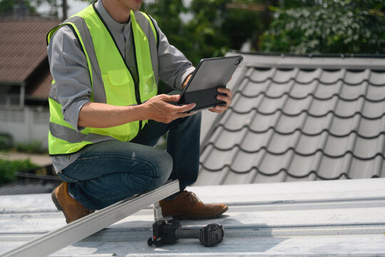 Close Up of Technician Preparing to Install Solar Panels on House Roof Using Digital Tablet for Planning