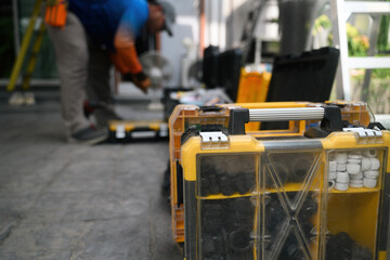 Fototapeta premium Yellow Plastic Tool Organizer Cases on Ground with Blurred Worker in Background at Outdoor Job Site