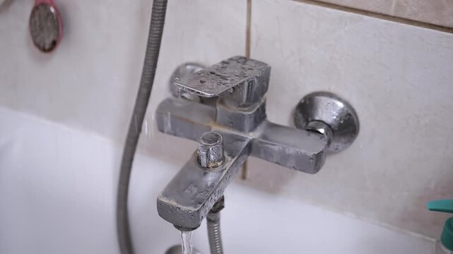 Water drips from a leaky, dirty, and rusty bathtub faucet. This highlights a common household plumbing problem, stressing the need for timely repair and maintenance to conserve water and