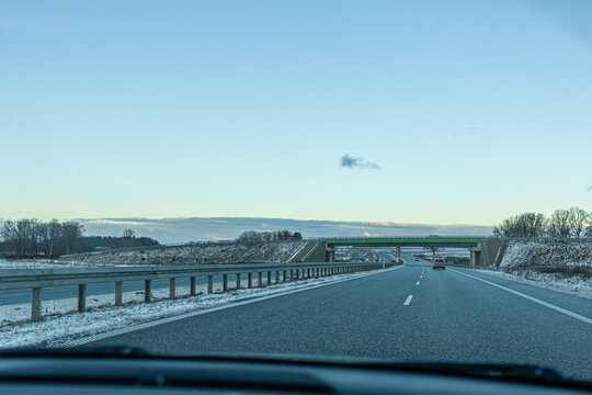 Modern Highway Infrastructure with Overpass Bridge in Winter Conditions. Multi-lane motorway passing beneath a modern overpass surrounded by snowy terrain. 