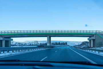 Multi-lane motorway passing beneath a modern overpass surrounded by snowy terrain. Strong transportation and engineering theme suitable for infrastructure projects. © Nadiia