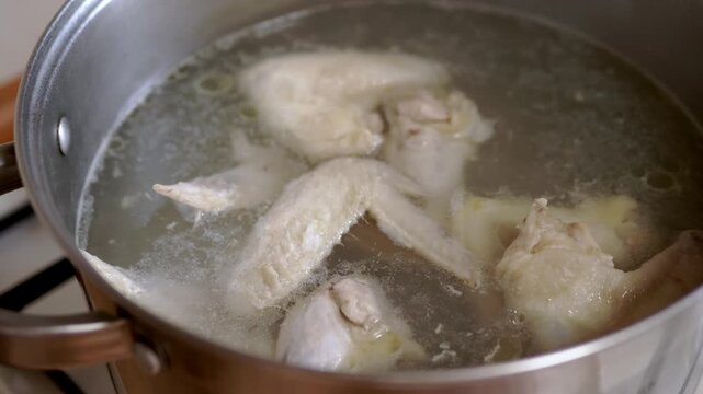 Close up, fresh chicken wings boil in water, perfect for delicious savory dishes and wholesome home meals. Captures the process of making chicken broth and soup. Slow motion.