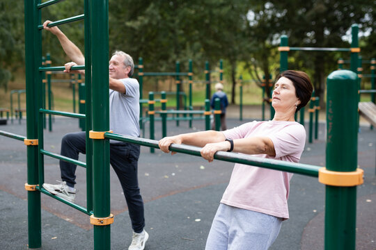 elderly man and woman perform exercises on horizontal bars at an outdoor sports ground