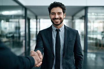 Fototapeta premium A smiling businessman in a suit shaking hands with another person inside a modern office with glass walls and bright lighting.