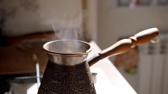 Steam rises from a traditional copper coffee pot with a wooden handle on a kitchen stove burner, capturing the concept of preparing fresh morning coffee in a slow motion sequence. The warm