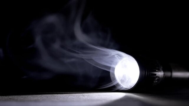 A bright flashlight lies on a dark surface illuminating swirling smoke with a sharp beam of white light. Concept of mystery, emergency search, and discovering hidden truths within the dark.