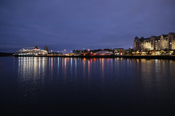 Fototapeta premium long-shot night view of Oslo Fjord harbor, city lights reflection of Oslo Havnelager and a cruise ship on the calm water surface
