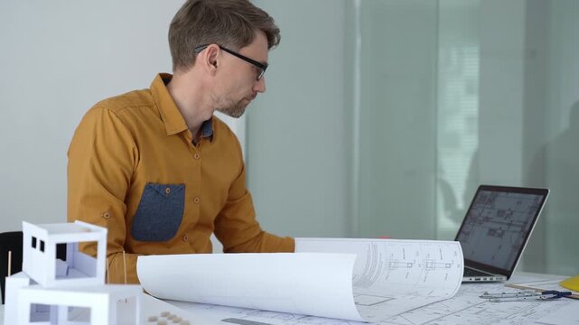 Architect carefully assembling a scaled architectural model, designing and planning a new building project on a desk with blueprints, engineering tools, and construction safety helmet