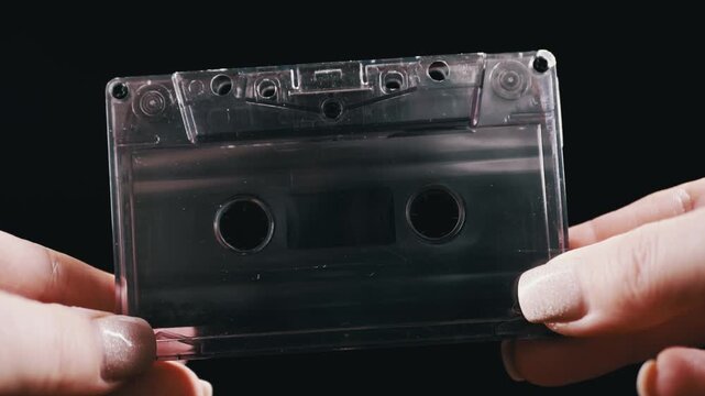Close up view of female hands holding a transparent vintage audio cassette tape against a dark background. Concept of retro music, nostalgic analog media, and vintage sound recording.