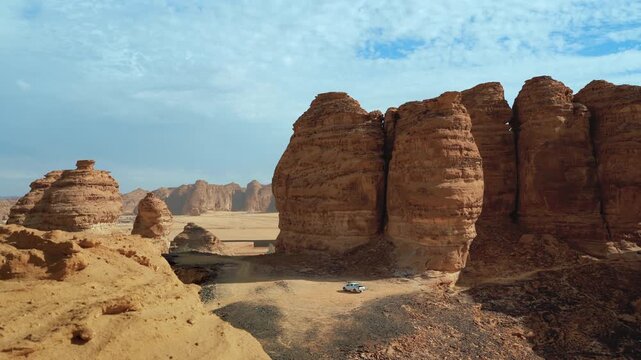 Sun shines to rocky desert landscape near Al Ula, view around from higher sandstone formation viewpoint near Vessel Hole Rock, small 4wd car in distance