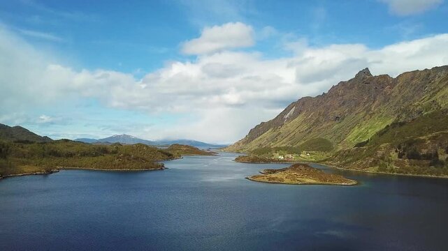 A wide view shows islands surrounded by water with mountains and trees in the background. The sun is shining and the sky is mostly clear. This area is located in Norway.