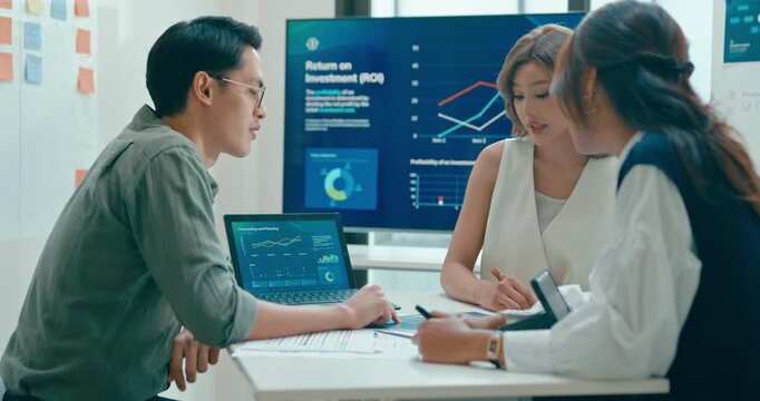 Group of Asian businesspeople work together discuss plan idea with investment data profit sale statistics in business meeting in office. Financial generation z team brainstorm on e-Commerce project.