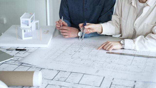 Engineering professionals collaborating on an architectural blueprint, using a compass to design a modern building, planning construction with a house model and laptop