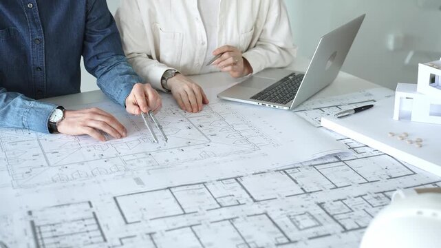 Architects and engineers collaborating on a housing project, designing building blueprints, planning new construction details, and discussing architectural models with a laptop on a desk