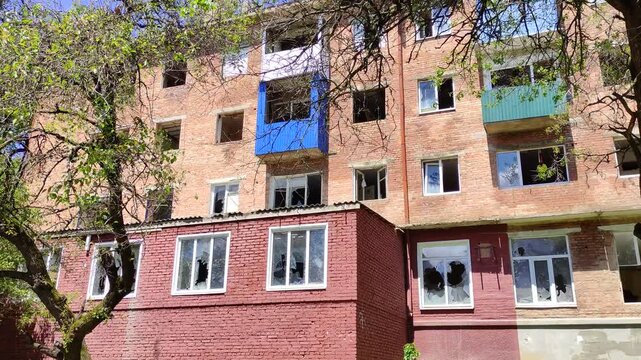 Abandoned weathered brick apartment building with blue balcony and broken windows