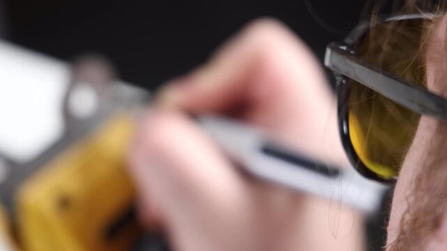 Extreme close up of a craftsman in yellow safety glasses with blurred hands soldering in background