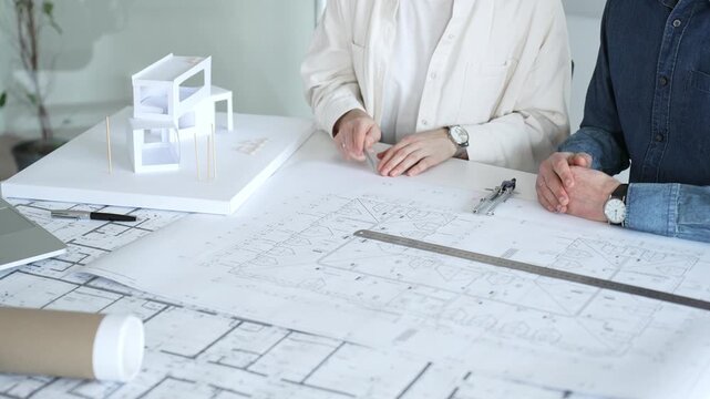 Engineering professionals collaborating on an architectural blueprint, using a compass to design a modern building, planning construction with a house model and laptop