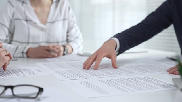 Business professionals reviewing contracts and paperwork in a meeting, pointing to key legal terms, negotiating and preparing signatures to finalize a collaborative agreement