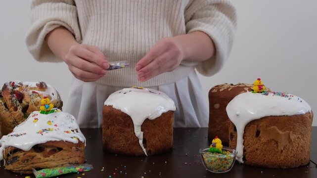 Woman dipping panettone into white icing and decorating Easter bread with colorful holiday sprinkles