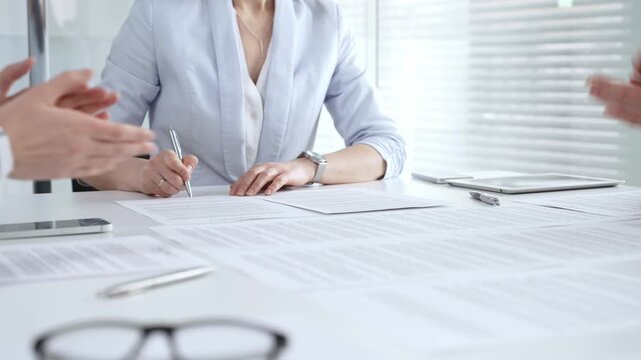 Businesswoman signing important contract documents at a meeting. Confirming agreement and partnership details while colleagues show support