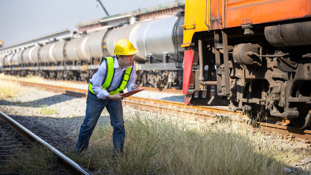 Professional engineer inspecting freight train at railway depot, Railway inspector checking cargo train maintenance on site, Industrial worker with safety gear examining train carriage at railroad