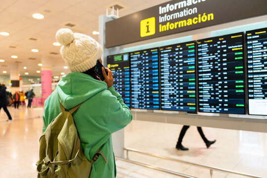 Traveler with backpack phoning while checking flight departure board information at airport terminal