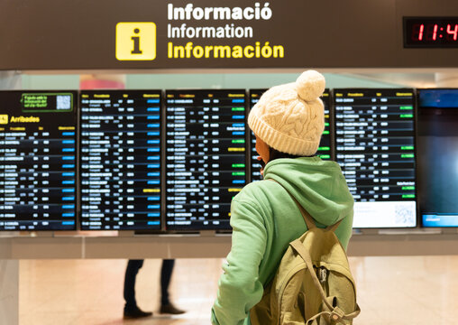 Traveler finding flight information on airport arrivals departure board, checking schedule for journeys and travel plans