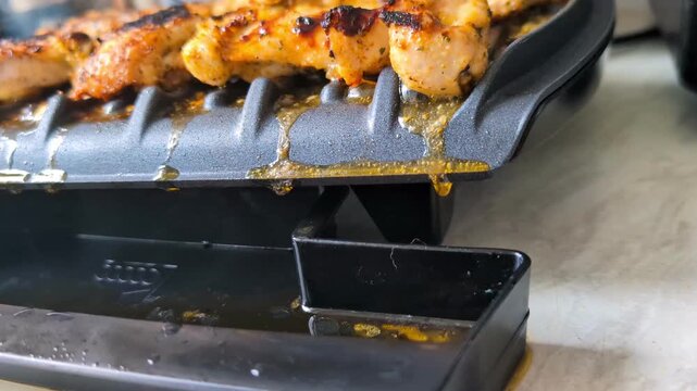 Close up chicken thigh on grill with fat dripping into tray during cooking process.