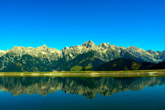 Ein gewaltiger Bergkamm in den Alpen spiegelt sich im ruhigen Wasser des vorgelagerten Bergsees.