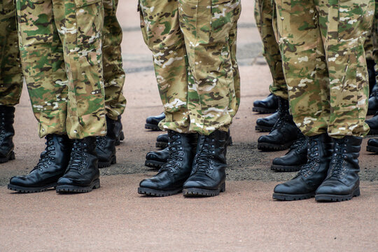 legs and feet of several soldiers standing in formation on an asphalt surface