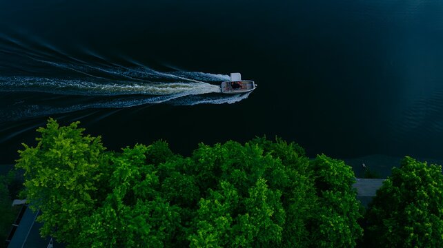 Aerial view of speedboat creating wake on dark water near green forest
