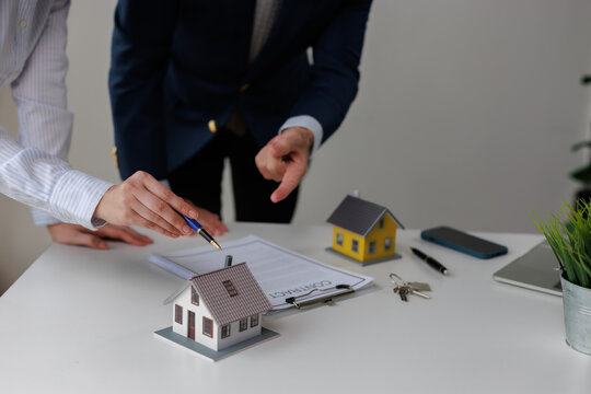 Real estate agent explaining purchase agreement terms to a client, pointing at a contract document for property investment or mortgage loan approval